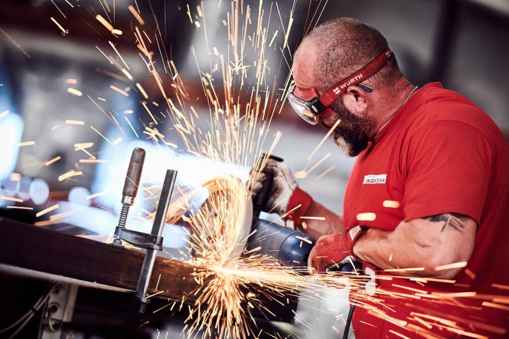 Mann schneidet mit einem Winkelschleifer ein Stück Metall, viele Funken sprühen.